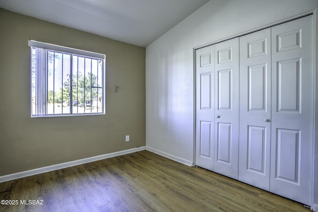 unfurnished bedroom with wood finished floors, baseboards, and a closet