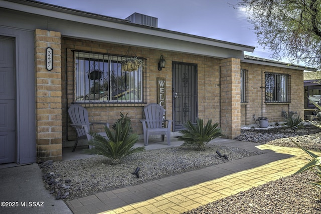 property entrance with central air condition unit, brick siding, and a porch