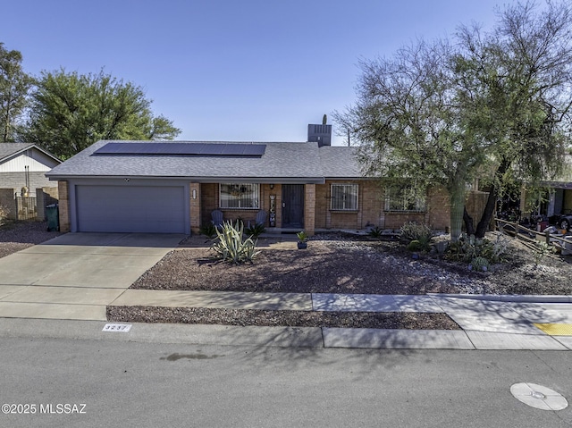 single story home featuring brick siding, solar panels, driveway, and a garage