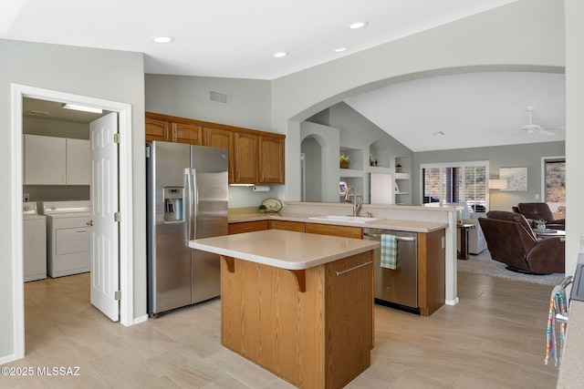 kitchen with lofted ceiling, stainless steel appliances, a center island, washing machine and clothes dryer, and kitchen peninsula