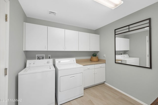 washroom featuring cabinets, washer and clothes dryer, and light hardwood / wood-style flooring