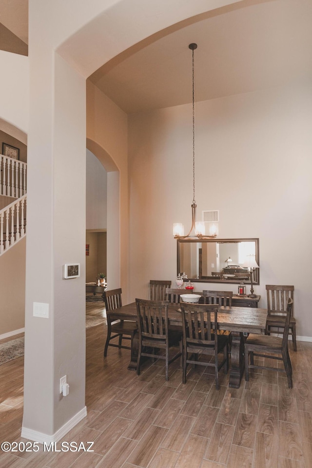 dining area with hardwood / wood-style flooring, a towering ceiling, and a notable chandelier