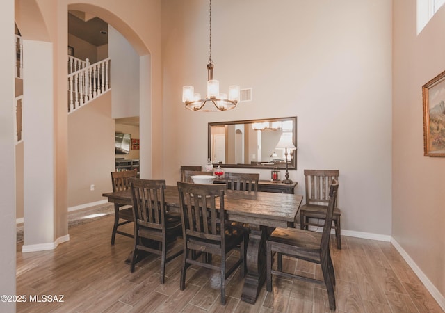 dining space with a towering ceiling, wood-type flooring, and a chandelier