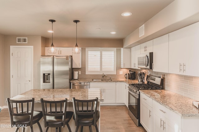 kitchen with a kitchen island, pendant lighting, white cabinetry, sink, and stainless steel appliances