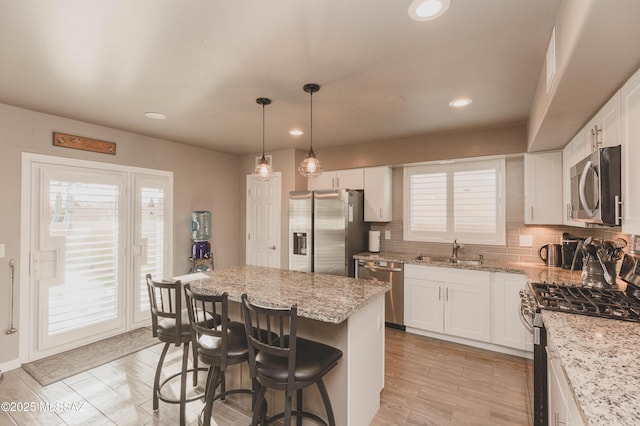 kitchen with a kitchen island, appliances with stainless steel finishes, white cabinetry, sink, and light stone countertops