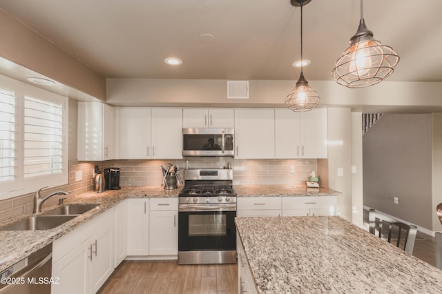 kitchen with appliances with stainless steel finishes, sink, hanging light fixtures, and white cabinets