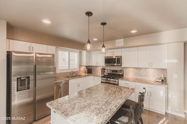 kitchen featuring hanging light fixtures, stainless steel appliances, a center island, and white cabinets