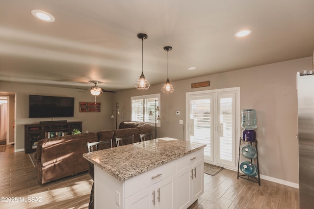 kitchen with a breakfast bar area, white cabinets, hanging light fixtures, a center island, and light stone countertops