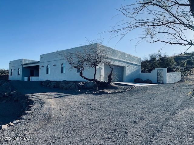 view of front facade with an attached garage, gravel driveway, and stucco siding