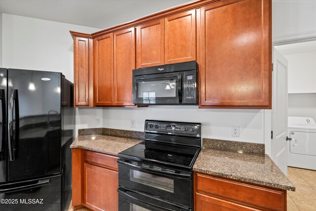 kitchen with light tile patterned flooring, dark stone countertops, washer / dryer, and black appliances