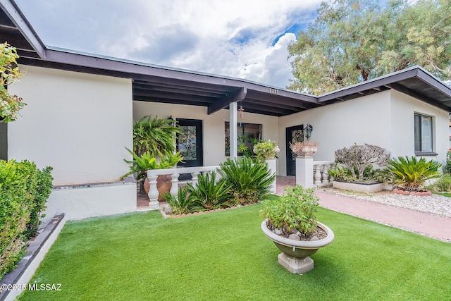 view of front of home with a front lawn, stucco siding, and covered porch