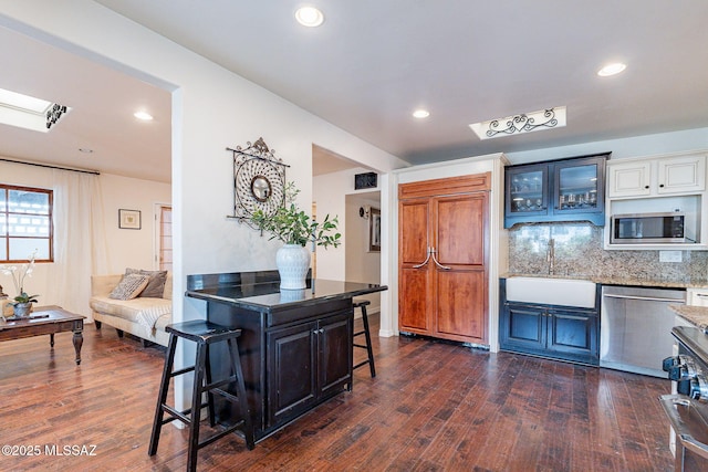 kitchen with a kitchen bar, tasteful backsplash, dark wood-type flooring, a sink, and built in appliances