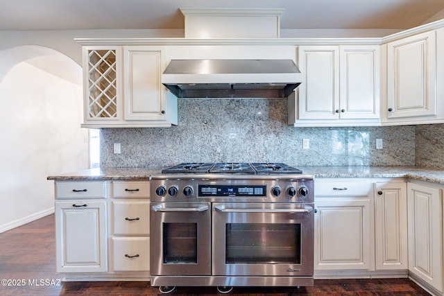 kitchen featuring dark wood finished floors, range with two ovens, wall chimney exhaust hood, and tasteful backsplash