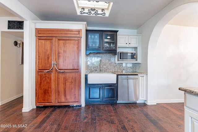 kitchen with tasteful backsplash, a sink, arched walkways, light stone countertops, and glass insert cabinets