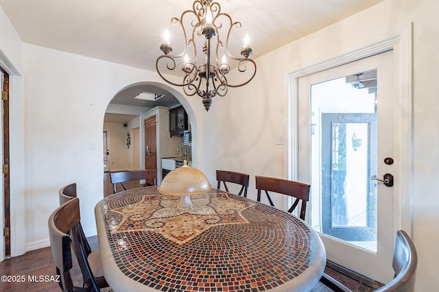 dining space featuring baseboards, wood finished floors, arched walkways, and an inviting chandelier
