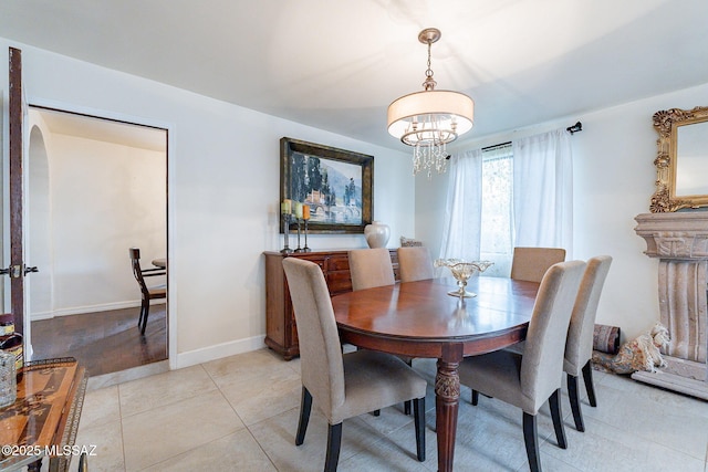 dining space with an inviting chandelier, light tile patterned floors, arched walkways, and baseboards