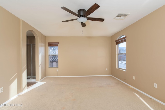 unfurnished bedroom featuring visible vents, arched walkways, multiple windows, and light colored carpet