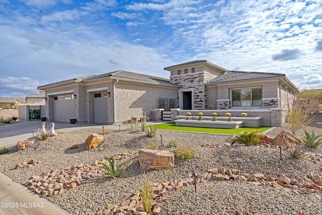 prairie-style house featuring driveway, stone siding, a tile roof, an attached garage, and stucco siding