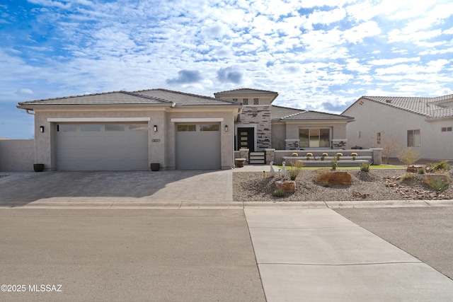 prairie-style home featuring decorative driveway, a tile roof, an attached garage, and stucco siding