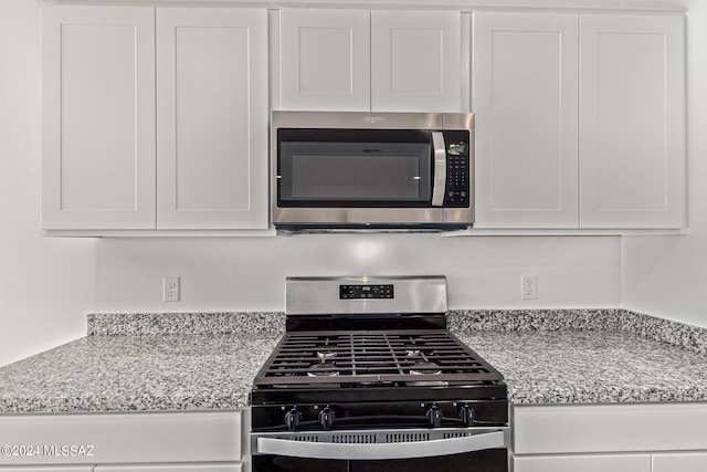 kitchen featuring gas range, light stone countertops, and white cabinets