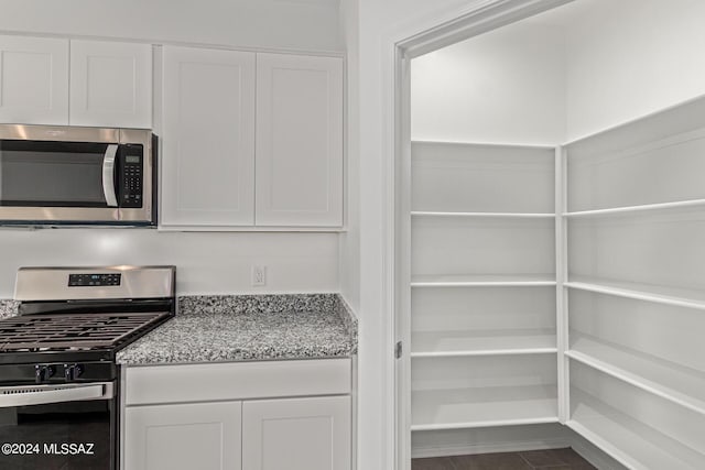 interior space featuring appliances with stainless steel finishes, light stone countertops, and white cabinets