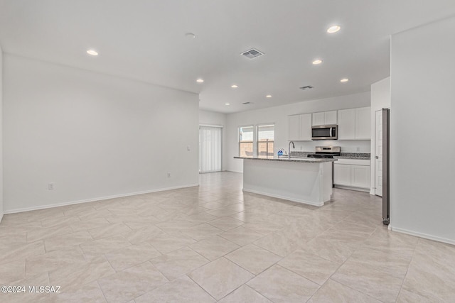 kitchen featuring sink, appliances with stainless steel finishes, white cabinetry, light stone counters, and a center island with sink