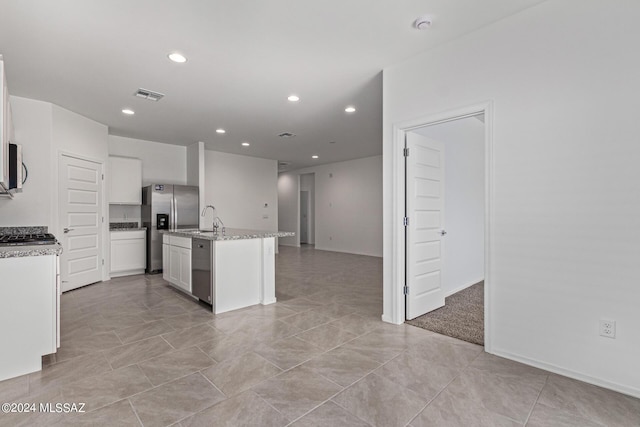 kitchen featuring sink, white cabinetry, a center island with sink, appliances with stainless steel finishes, and light stone countertops