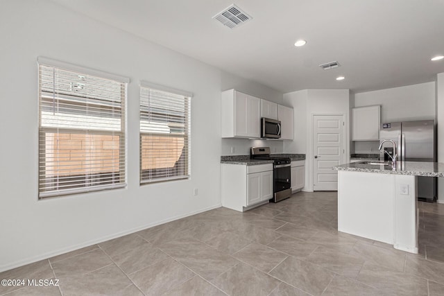 kitchen featuring a kitchen island with sink, light stone counters, white cabinetry, and appliances with stainless steel finishes