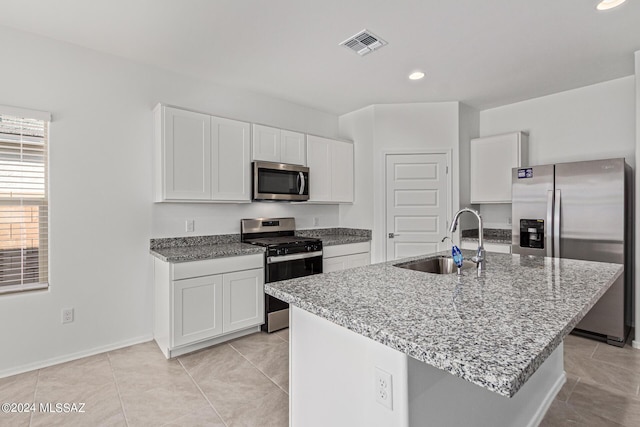 kitchen featuring appliances with stainless steel finishes, an island with sink, sink, white cabinets, and light stone counters