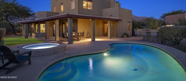 pool at dusk with an in ground hot tub, area for grilling, exterior bar, and a patio