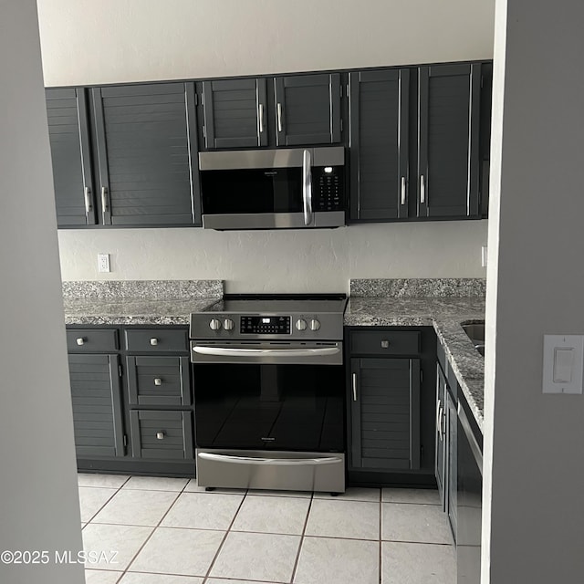 kitchen featuring light tile patterned floors, stainless steel appliances, dark stone counters, and dark cabinets