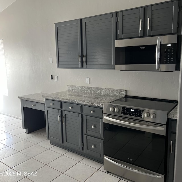 kitchen with stainless steel appliances, gray cabinets, light tile patterned flooring, and a textured wall