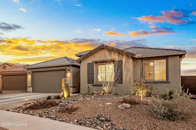 view of front of house featuring driveway, an attached garage, a tile roof, and stucco siding