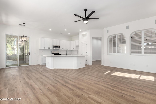 kitchen featuring appliances with stainless steel finishes, decorative light fixtures, light hardwood / wood-style floors, ceiling fan with notable chandelier, and white cabinetry