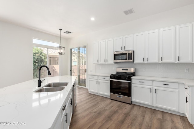 kitchen with appliances with stainless steel finishes, sink, light hardwood / wood-style flooring, white cabinets, and hanging light fixtures