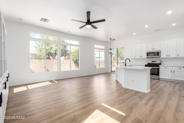 kitchen with appliances with stainless steel finishes, a center island with sink, light wood-type flooring, pendant lighting, and sink