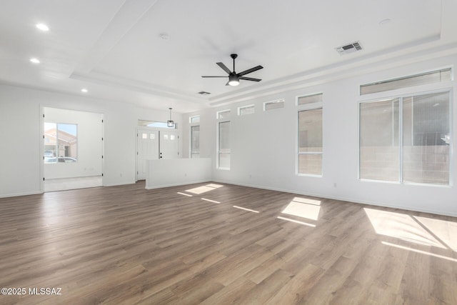 unfurnished living room featuring ceiling fan, a raised ceiling, and wood-type flooring