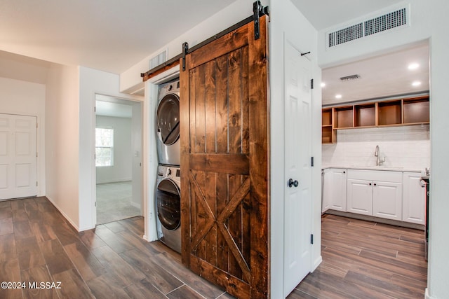 laundry area featuring sink, dark wood-type flooring, stacked washer and clothes dryer, and a barn door