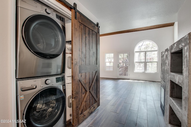 laundry area featuring a barn door, a textured ceiling, and stacked washer / dryer