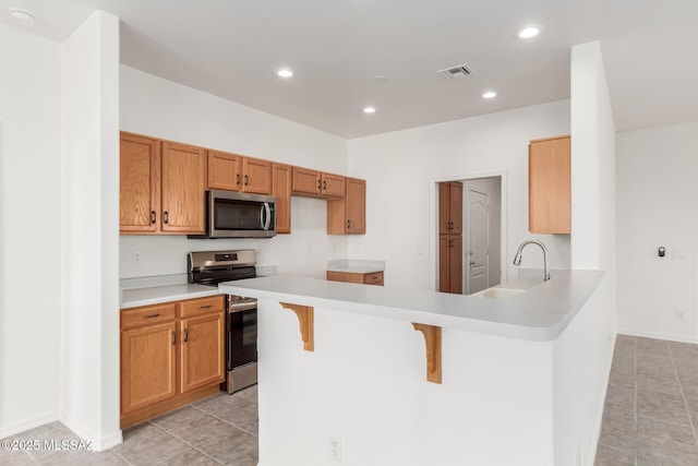 kitchen with light tile patterned floors, sink, stainless steel appliances, a kitchen bar, and kitchen peninsula