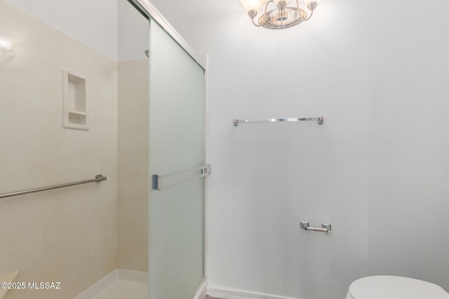 bathroom featuring an inviting chandelier, a shower with shower door, and toilet