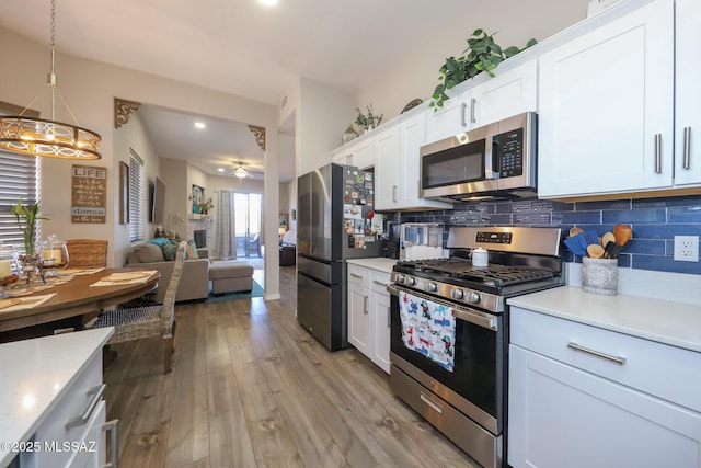 kitchen featuring appliances with stainless steel finishes, pendant lighting, tasteful backsplash, white cabinets, and light wood-type flooring