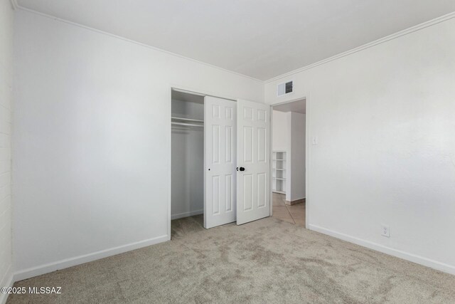 unfurnished bedroom featuring crown molding, light colored carpet, and a closet