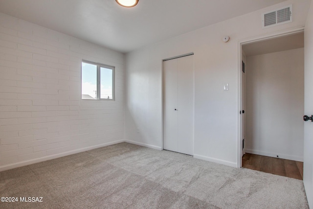 unfurnished bedroom with light colored carpet, a closet, and brick wall