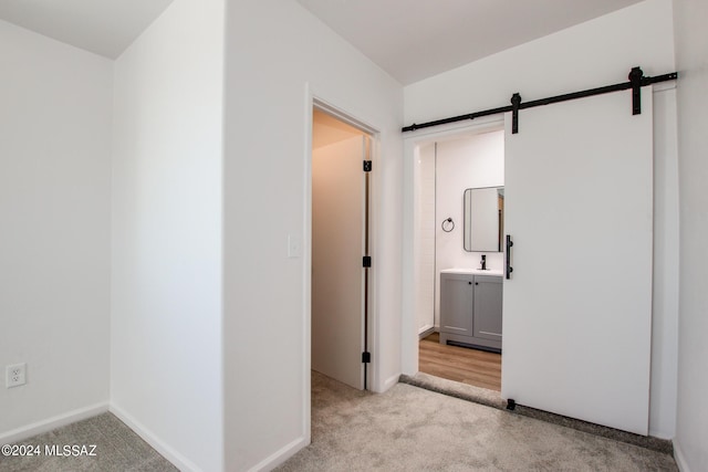 corridor with a barn door, sink, and light carpet