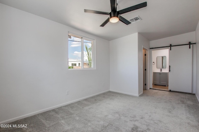 unfurnished bedroom featuring ensuite bathroom, a barn door, and light colored carpet