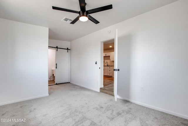 interior space featuring a barn door, sink, light colored carpet, and ceiling fan