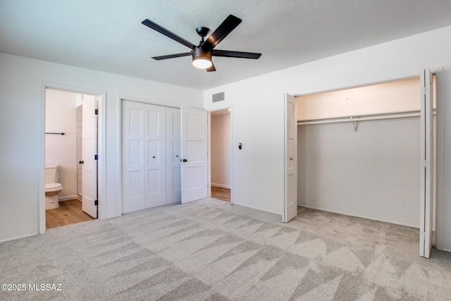 unfurnished bedroom with carpet, multiple closets, visible vents, a ceiling fan, and connected bathroom