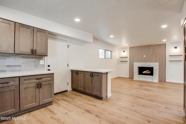 kitchen featuring light wood-style flooring, open floor plan, a peninsula, light countertops, and backsplash