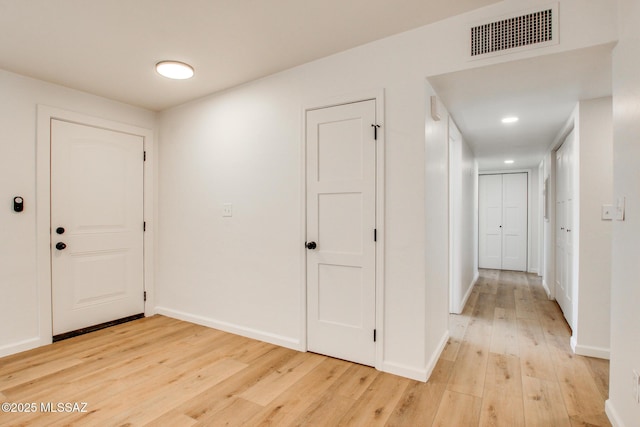 hallway with light wood-type flooring, visible vents, and baseboards